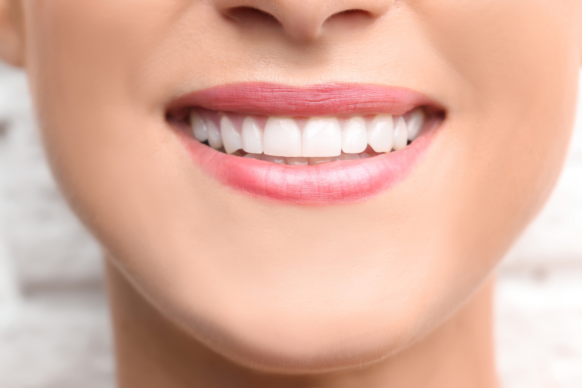 Young beautiful woman with healthy teeth smiling on light background, close up